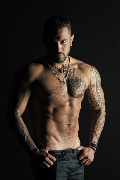 Sportsman con sei pack e addominali stripping. Uomo spogliarellista mostra busto sexy. Atleta con muscoli bicipiti e tricipiti. Uomo di moda con tatuaggio decollare jeans. Desiderio di sessualità e attrazione — Foto Stock