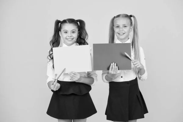 Πίσω στη σχολική διαφήμιση. Χαρούμενα παιδιά στο σχολείο που δείχνουν κενά φύλλα σε κίτρινο φόντο. Μικρά παιδιά ξεκινούν νέα σχολική χρονιά. Μικρά κορίτσια που κρατούν κενές σχολικές αφίσες για κείμενο, αντιγραφή χώρου — Φωτογραφία Αρχείου
