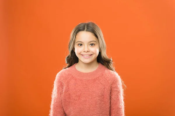 self-confidence portrait. small kid autumn sweater. feel comfortable in casual fashion. child orange background. carefree childhood. her healthy smile. happy childrens day. cute little girl smiling