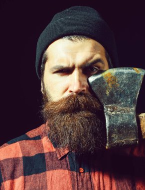 Şapkalı yakışıklı sakallı adam siyah arka planda balta tutuyor.