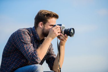 Adam açık havada gökyüzü arka planında. Yakışıklı blogcu, gezgin, geçmişe dönük kamera. Elle ayarlar. Gezgin blogcu. Antika ekipmanlar. Gazeteci fotoğraf çekiyor. Hippi fotoğrafçı. Blogger vurucu vlog