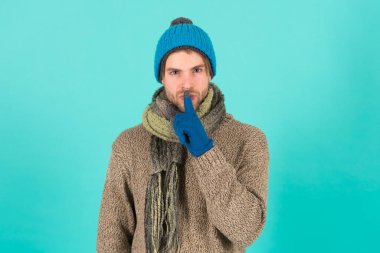 Sırrımı sakla. Tıraşsız yakışıklı adam mavi arka planda kış aksesuarları takıyor. Kış sezonu indirimi. Hippi, kış şapkası eşarbı ve eldiven ördü. Duygusal bir ifade. Gizemli bir anlaşma. Dilek listesi