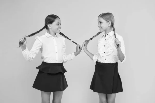 Cabelo fácil de fazer você mesmo. Meninas adoráveis com cabelos entrançados no fundo amarelo. Bonito crianças pequenas segurando tranças de cabelo longas. Trança e styling cabelo para a escola — Fotografia de Stock