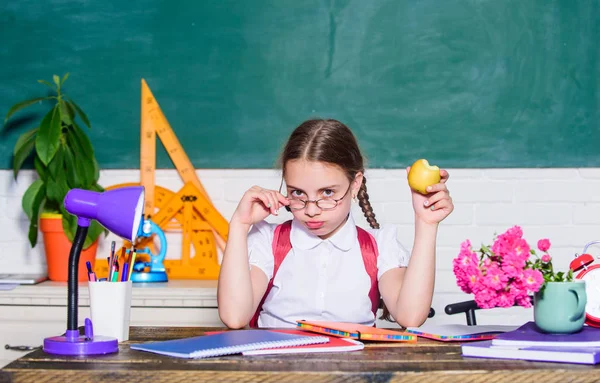 Student na škole. Školačka sedět stůl tabuli pozadí. Holčička jí jablečnou svačinku. Školní prázdniny. Klid mezi lekcemi. Vitaminová náplň. Školní životní koncept. Zdravý životní styl — Stock fotografie