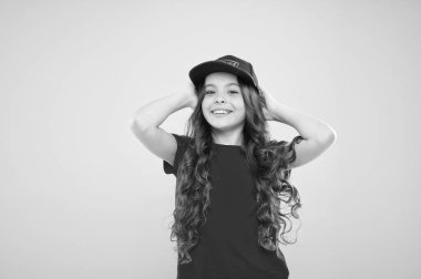 Yaz güneşi koruma şapkası. Uzun kıvırcık saçlı bir kız şapka takıyor. Sokak tarzı aksesuarları olmalı. Modern moda. Çocuk modası. Sevimli çocuk şapkası takıyor ya da şapkası takıyor. Beyzbol şapkası takan küçük kız