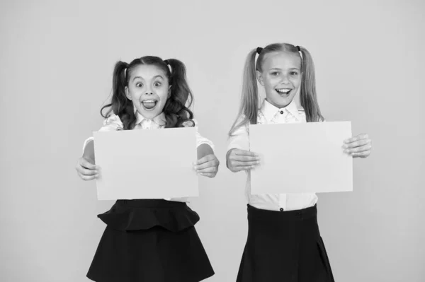 Idea publicitaria para la escuela. Chicas felices sosteniendo hojas de papel para cierta idea sobre fondo amarillo. Pequeños niños lindos sonriendo de idea genio. Niños pequeños con papel vacío para su idea, espacio para copiar —  Fotos de Stock