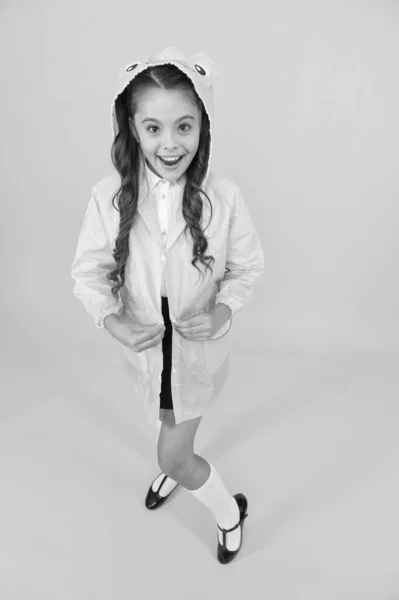 Fácil sujeción. Feliz colegiala saliendo sobre fondo amarillo. Pequeña colegiala vestidor impermeable y capucha para el día de lluvia. Pequeña colegiala sintiéndose protegida por el clima otoñal —  Fotos de Stock