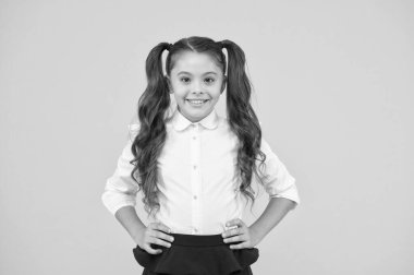 Okula hoş geldin. Sevimli gülümsemeile küçük bir okul çocuk. Küçük bir okul çocuğu sarı arka planda gülümsüyor. Mutlu küçük kız okula dönüyor. Resmi giyim uzun esmer saçlı sevimli küçük çocuk