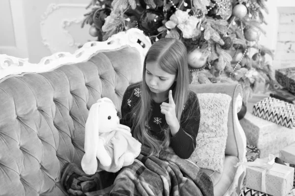 私に耳を傾ける必要があります。小さな女の子は、クリスマス ツリー、かわいいウサギを教えます。柔らかいおもちゃまで少し子ポインティング指。小さな女の子は、うさぎグッズを保持します。現在の小さな子。最高のクリスマスのおもちゃ — ストック写真