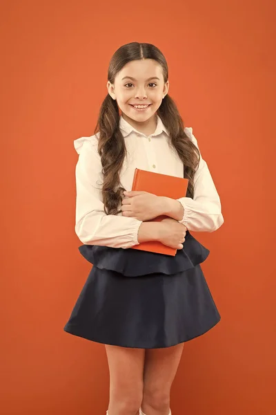 Homeschooling concept. get information form book. small girl in school uniform. diary for making notes. schoolgirl writing notes on orange background. home schooling for little girl. happy schoolgirl