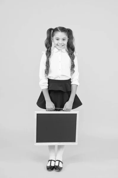 Preparando a un niño pequeño para la escuela. Niña sosteniendo pizarra negra sobre fondo amarillo. Niño pequeño con pizarra vacía para tu texto. Pequeño escolar sosteniendo pizarra para publicidad, espacio de copia —  Fotos de Stock