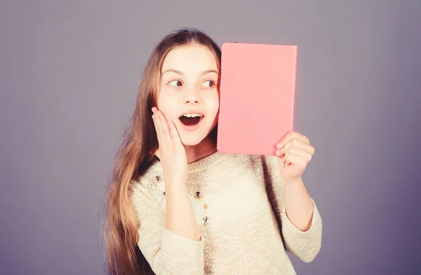 Door onderwijs te verbeteren. Verrast klein meisje met open mond Holding onderwijs boek met Rosy cover. Schattig klein kind krijgt formeel onderwijs in de lagere school. Onderwijs, kopieerruimte — Stockfoto