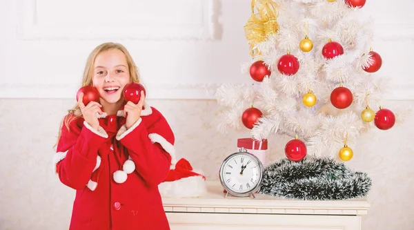 Parte favorita de decoração. Envolver a criança na decoração. Menina sorridente rosto segurar bolas ornamentos fundo interior branco. Como decorar a árvore de Natal com a criança. Deixe a criança decorar árvore de Natal — Fotografia de Stock