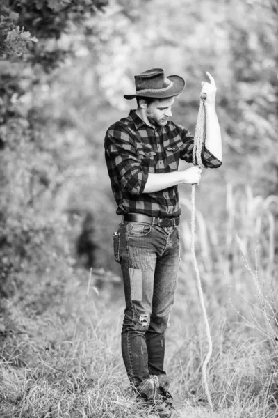 Cowboy no campo. Homem de chapéu segura corda. Ocupações no rancho. Ferramenta de laço. Cowboy americano. Laço amarrado embrulhado. A vida ocidental. Homem cowboy natureza fundo. Dono do rancho. Seattle conceito de reprodução — Fotografia de Stock