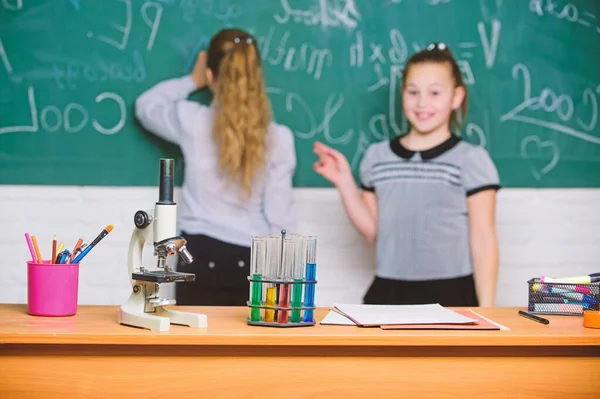 Microscoop en reageerbuisjes op tafel. Chemische reacties. Maak het bestuderen van chemie interessant. Leerling op schoolbord op scheikunde les. Educatief experiment concept. Meisjes klasgenoten studie chemie — Stockfoto