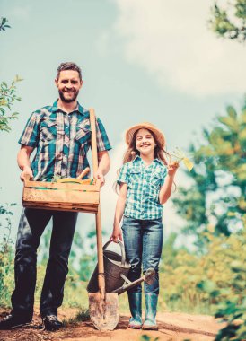 Baba ve kızı çiftlikte. Yaz çiftçiliği. Çiftçi adam ve küçük kız. Bahçe aletleri, kürek ve su kovası. Babasıyla çalışan bir çocuk. Aile bağı. Spring Country Side Köyü. Çiçek sulama