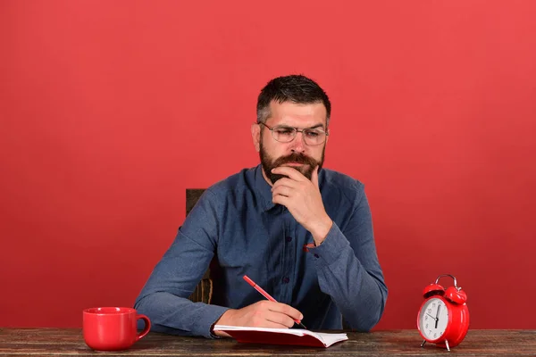 Hombre con barba, gafas escribe en cuaderno sobre fondo rojo —  Fotos de Stock