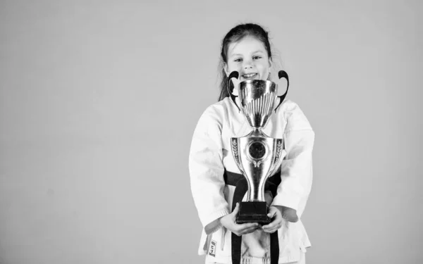 Knockout. energy and activity for kids. winner little girl in gi sportswear. small girl with champion cup. martial art. practicing Kung Fu. happy childhood. sport success in single combat. copy space — Stock Photo, Image