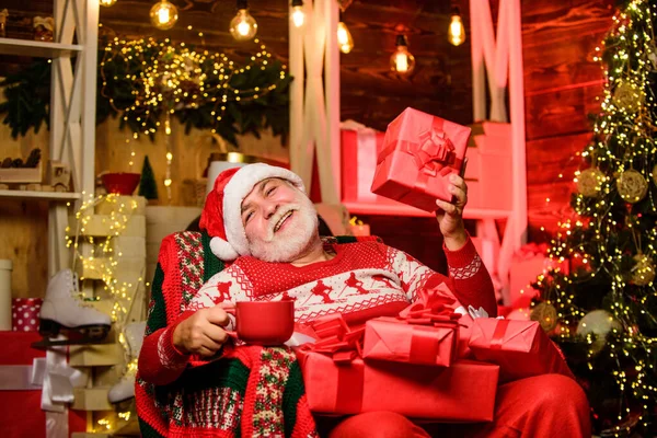 Entregar presentes. Pai Natal perto da árvore de Natal. Feliz Natal! Feliz Natal! Papai Noel, um idoso barbudo. Papai Noel relaxando em cadeira de braço. Férias de inverno. Avô idoso em casa. Conceito de tradições — Fotografia de Stock