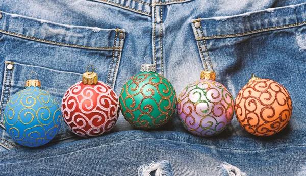Christmas decorations concept. Pick colorful decorations. Modern christmas decor. Balls with glitter and shimmering decorative ornaments. Christmas ornaments or decorations on denim pants background — Stock Photo, Image
