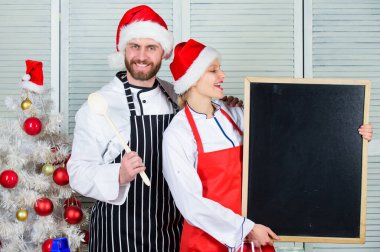 Erkek ve kadın şef Noel Baba şapkası Noel ağacının yanında. Noel tarifi kavramı. Çift, Noel yemeği için birlikte sağlıklı vejetaryen yemeği hazırlıyor. Gizli bileşen aşktır. Noel yemeği pişiriyorum.