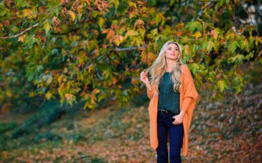 Hafta sonu için samimi kıyafet fikirleri. Kadın gün batımında yürüyor. Sonbaharda giymek için rahat kıyafetler. Rahat bir kıyafet. Sevimli sarışın kız, sıcacık ve rahat pozlar veriyor. Sonbahar doğasının arka planı çözüldü.