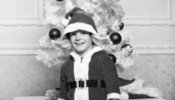 Chłopiec dziecko ubrany jak Ładna elf magiczną istotę biały sztucznych uszy i red hat w pobliżu choinki. Boże Narodzenie elf kostium dla dziecka. Przyjęcie bożonarodzeniowe z elf kostium. Choinka pomysły dla dzieci — Zdjęcie stockowe