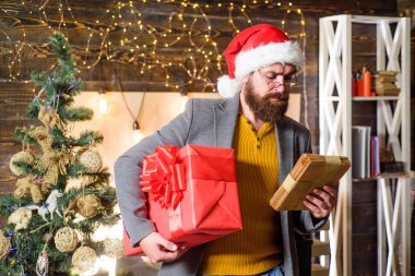 Noel ruhu burada. Sakallı adam Noel Baba şapkası takıyor ve hediye kutusu taşıyor. Teslimat, yılbaşı hediyesi. Noel hediyesi. Noel Baba şapkalı adam hediyesi. Teslimat servisi. Mutluluk ve neşe saçın