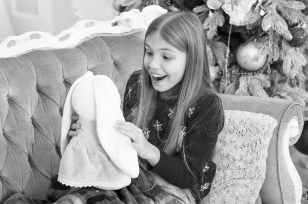 Feliz Ano Novo. Criança pequena feliz sorrindo para apresentar. Menina com coelhinho bonito na árvore de Natal. Menina pequena segurar brinquedo de coelho. Pequena criança brincar com brinquedo macio. Melhor brinquedo de Natal — Fotografia de Stock