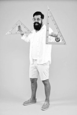 Çiziminiz için ihtiyacınız olan araçlar. Geometri veya teknik çizim öğretmeni. Sakallı adam sarı arka planda çizim aletleri tutuyor. Mühendislik çizimi yapmak için üçgen kullanan mühendis