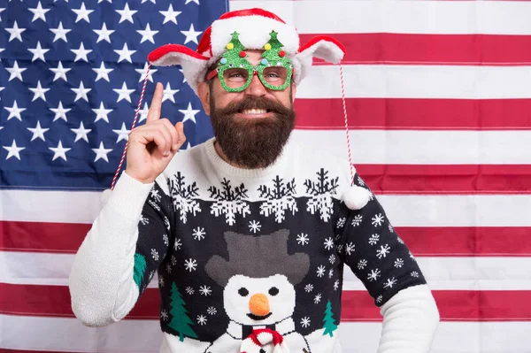 Firandet börjar med idé. Glad tomte håller fingret högt. Skäggig man ler i vinterstil. Festlig vinterfest. Vintersäsong. Vinterlov. Julen. Nytt år. Amerikansk flagg bakgrund — Stockfoto