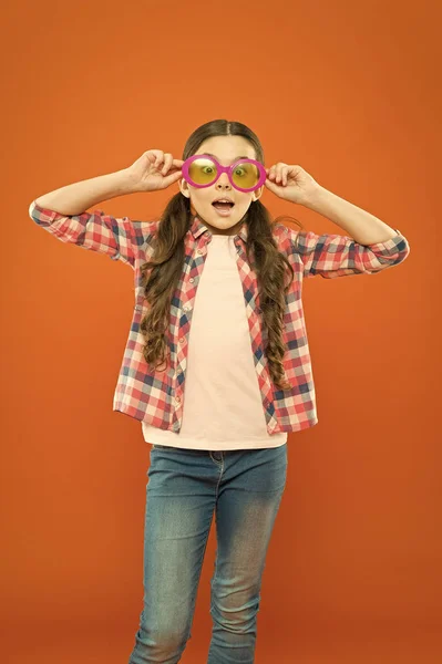 Натякай це смішно. Маленька дівчинка дивиться через кумедні окуляри з кольоровим фільтром на помаранчевому фоні. Забавна дитина носить сонцезахисні окуляри на здивованому обличчі. Мої очі смішні — стокове фото