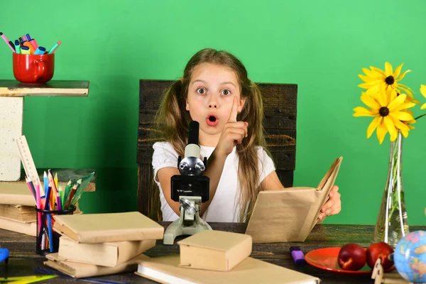 Школа сидит за столом с красочными канцелярскими принадлежностями, книгами и микроскопом — стоковое фото