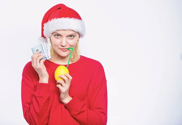 财富和丰富的象征。有钱的女孩用柠檬和钱。柠檬钱的概念。女孩圣诞老人帽子喝果汁柠檬, 而持有桩钱。用新鲜的柠檬水赚钱。圣诞节利润概念 — 图库照片