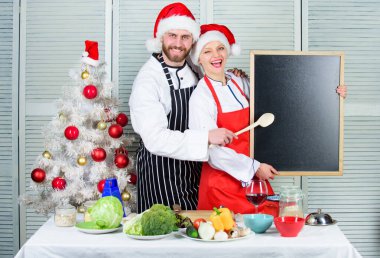Noel tarifi kavramı. Ailemiz için menü. Erkek ve kadın şef Noel Baba şapkası Noel ağacının yanında karatahta fotokopi alanı tutuyor. Çiftler yılbaşı yemeği için birlikte yemek tarifi okurlar. Noel yemeği pişiriyorum.