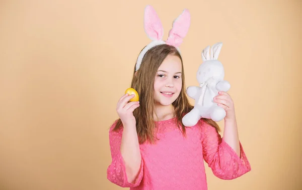 Девочка маленькая девочка пасхальный кролик аксессуар держать окрашенное яйцо. Происхождение пасхального кролика. Пасхальные символы и традиции. Игривый ребенок с мягкой игрушкой. Встречайте весенний праздник. Охота за пасхальными яйцами в рамках фестиваля — стоковое фото