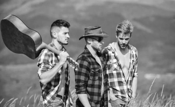 Group of young people in checkered shirts walking together on top of mountain. Men with guitar hiking on sunny day. Tourists hiking concept. Hiking with friends. Long route. Adventurers squad