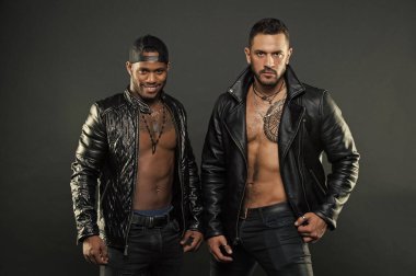 Seksi kıl ve geometrik dövme göğsüne İspanyol adamla. Beyzbol kap gülümseyen Afrika adam. Modelleri kas torsolar giyen deri ceket ve moda aksesuarları, moda kavramı ile