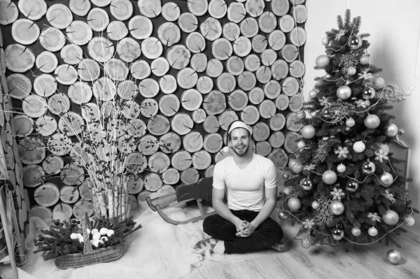Mannen i santa hatt sitta på golvet vid julgran — Stockfoto