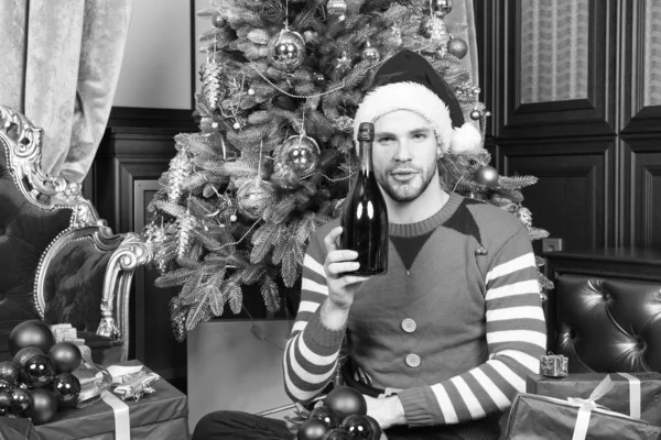Hombre en sombrero de santa con botella de champán en el árbol de Navidad — Foto de Stock