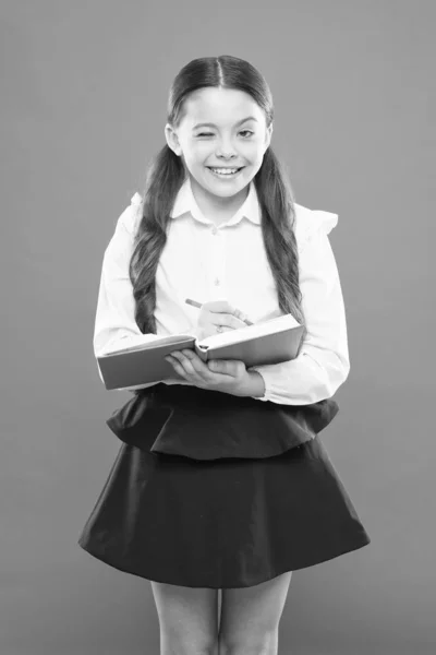 Colegiala escribir notas sobre fondo naranja. Niña con uniforme escolar. colegiala sosteniendo libro de lecciones. obtener información libro de formularios. de vuelta a la escuela. linda chica mantenga bloc de notas o diario. Diario para niña — Foto de Stock