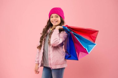 Alışverişte gündelik görünüşünü geliştir. Alışveriş torbalarını tutan mutlu kız. Küçük çocuk alışverişi sever. Şirin, küçük, pembe bir arka plan. Sonbahar indirimi. Alışveriş onun hayatı.