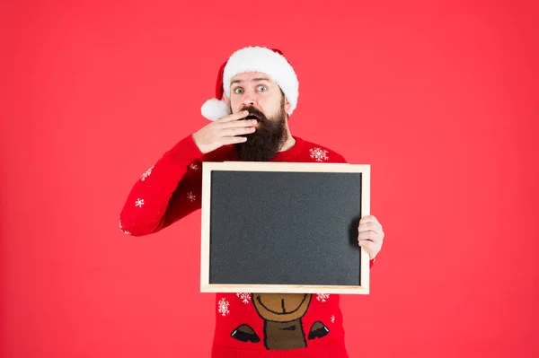 Inacreditável. Anúncio de inverno. Evento de inverno. Férias de inverno. Chapéu de Papai Noel com propaganda. Chalkboard para informação. Homem segurar espaço de cópia de quadro-negro em branco. Guy santa claus fundo vermelho — Fotografia de Stock