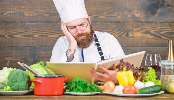 Receta para cocinar alimentos saludables. Receta vegetariana. Chef experimentado cocina excelente plato. Esta receta es perfecta. Hombre barbudo hipster leer libro receta cerca de verduras frescas de mesa. Artes culinarias — Foto de Stock