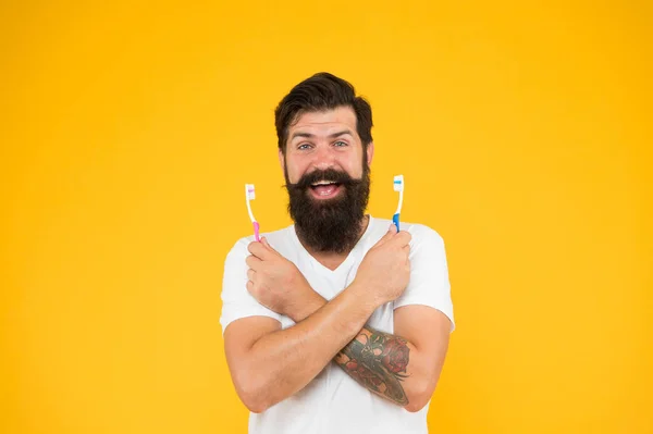 歯のホワイトニング手順。超音波歯の洗浄技術。髭の男は歯ブラシの黄色の背景を持っています。歯ブラシを２本持ってるヒップスター幸せな笑顔衛生を気にします。歯ブラシ — ストック写真
