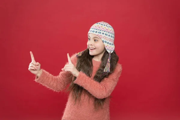 Puntando in questo modo. Vestito invernale. Modello carino godere di stile invernale. Piccolo bambino capelli lunghi indossare cappello sfondo rosso. Concetto invernale. Il bambino indossa un cappello a maglia. Ragazzina inverno accessori moda — Foto Stock