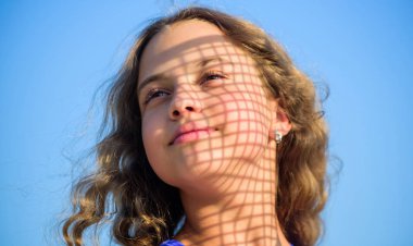 Yaz bakımı. Kız dışarıda dinleniyor. Kendine iyi bak. Uv filtresi güneş kremi. Güneş kremi. Sıcak güneş ışığından memnun olan çocuk rahat mavi gökyüzü arka planına benziyor. Kendine iyi bak. Güneş kremi sür.