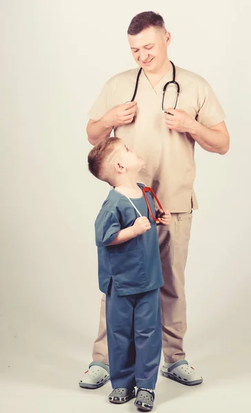 Θέλω να γίνω γιατρός ως μπαμπάς. Χαριτωμένο παιδί παίζουν το παιχνίδι του γιατρού. Οικογενειακός γιατρός. Παιδίατρος. Πατέρας γιατρός με στηθοσκόπιο και μικρή στολή γιου γιατρού. Ιατρική και υγειονομική περίθαλψη. Μελλοντικό επάγγελμα — Φωτογραφία Αρχείου