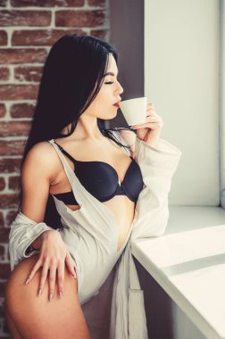 Sabahları kahve ona keyif veriyor. Şehvetli kız sabah kahvesinin tadını çıkarıyor. Pencerede sağlıklı bir sabah içkisi içen seksi kadın. Kahve onu sabah uyandırır.