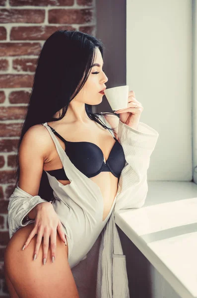 Koffie in de ochtend geeft haar de stemming. Sensueel meisje geniet van haar aromatische ochtendkoffie. Sexy vrouw die gezonde ochtenddrank drinkt bij het raam. Koffie maakt haar wakker in de ochtend. — Stockfoto